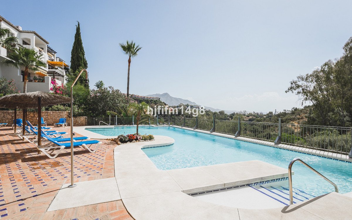 Resort swimming pool with lounge chairs and umbrellas, overlooking a scenic mountain landscape under a clear blue sky.