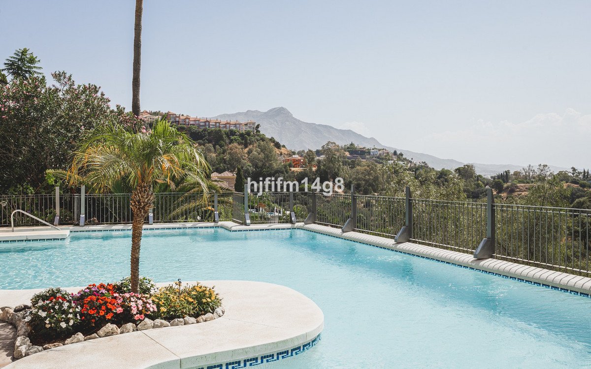 Swimming pool with a palm tree and colorful flowers, overlooking a picturesque mountain landscape.