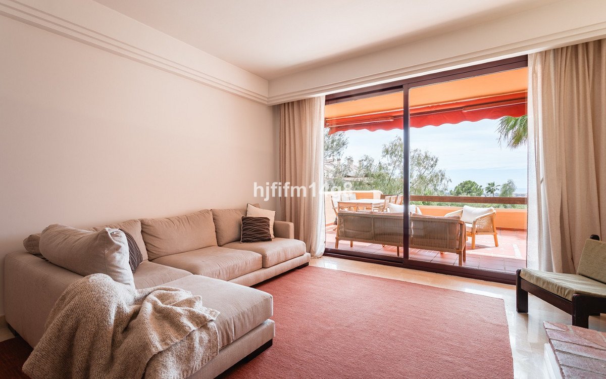 A spacious living room with a large sectional sofa, leading to a sunny terrace with seating and a scenic view.