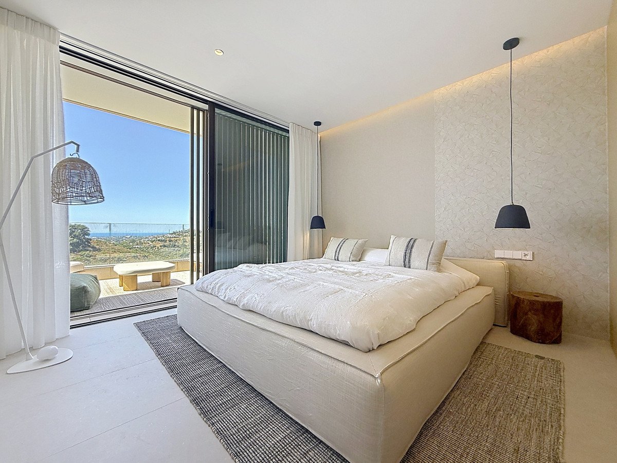 Modern bedroom with a large bed, floor lamp, and sliding glass doors opening to a balcony with a sea view.