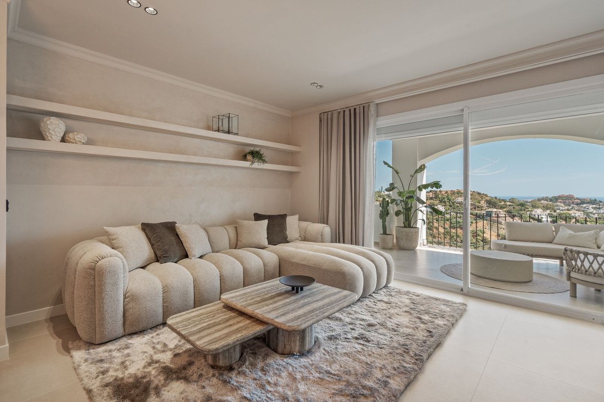A modern living room with a large sectional sofa, coffee table, and balcony with a sea view and outdoor seating.