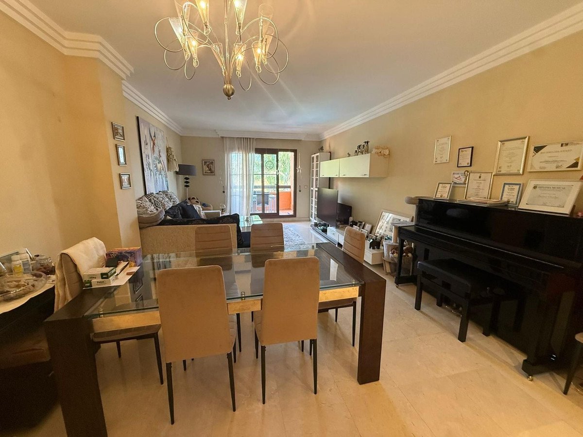 A spacious living and dining area featuring a grand piano, a dining table with chairs, and a sofa in the background.