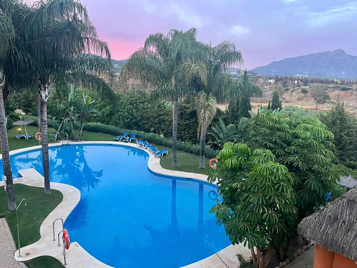 A swimming pool with lounge chairs and palm trees, overlooking hills and mountains at sunset.
