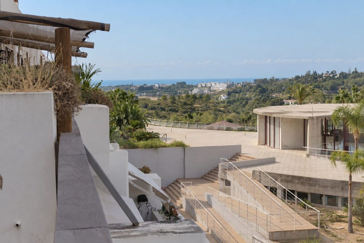 Terrace with a view of the sea and surrounding green hills, featuring modern architecture and outdoor spaces.