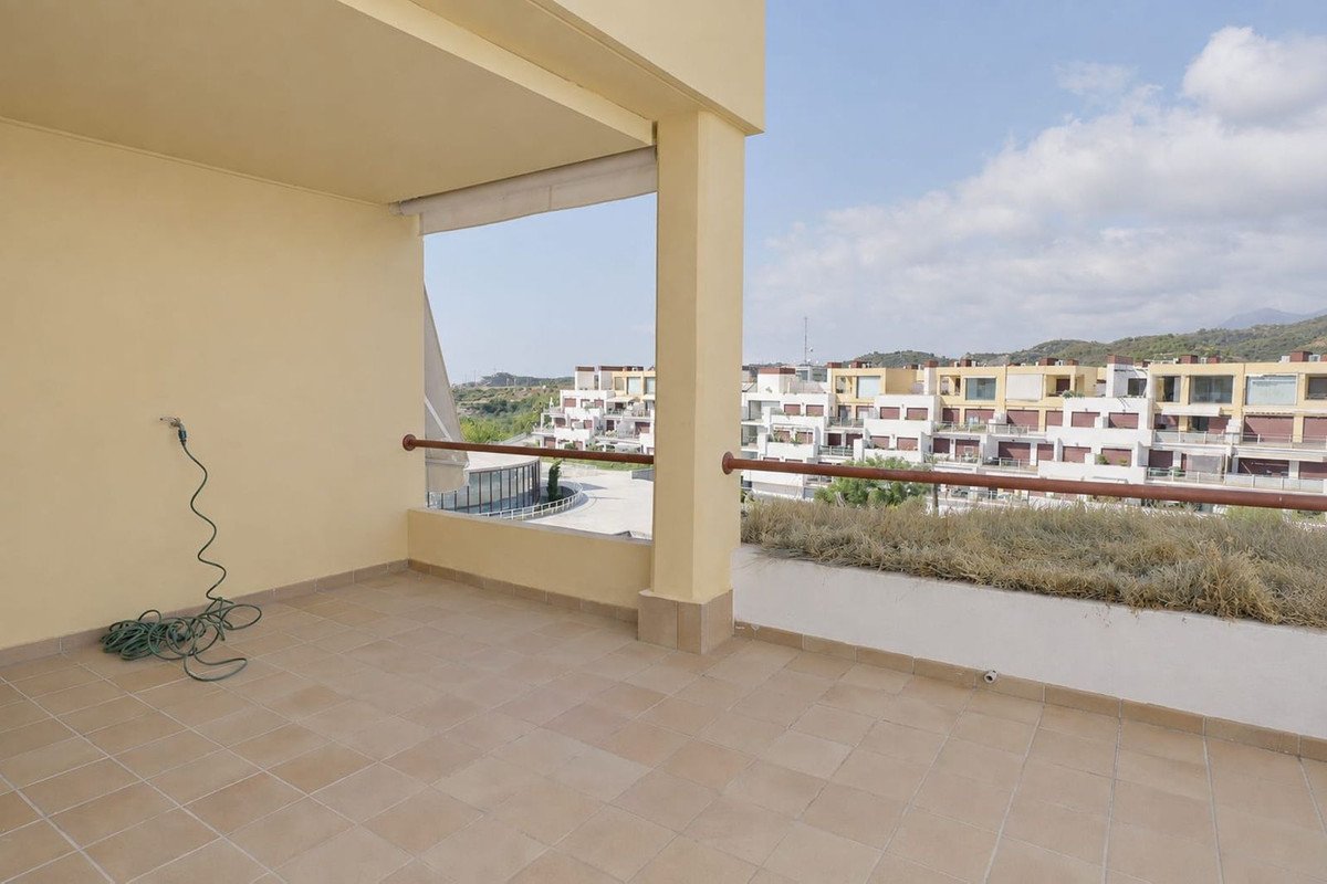 Spacious tiled terrace with railings and a view of apartment buildings and distant hills under a cloudy sky.