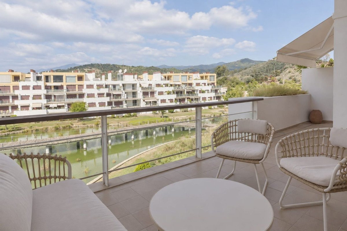 Terrace with seating overlooking a tranquil water feature and a modern apartment complex with hills in the background.