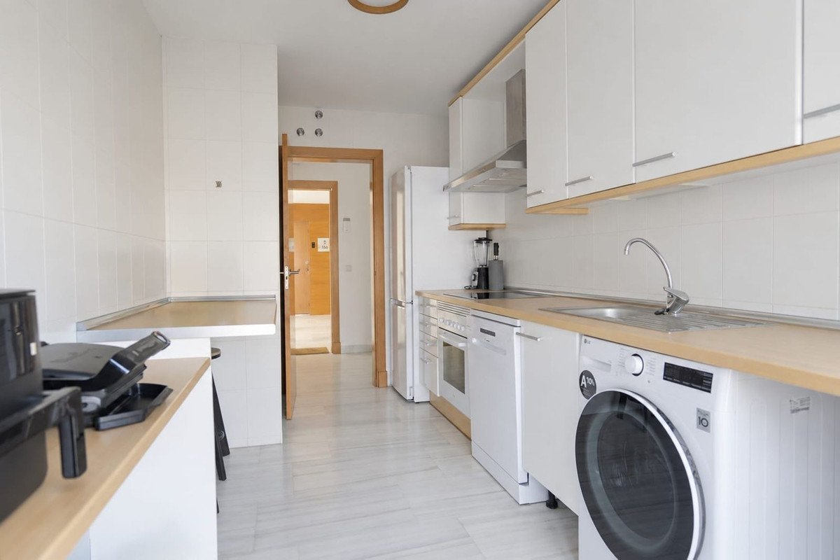 A modern white kitchen with light wood countertops, stainless steel appliances, and a washer-dryer unit.
