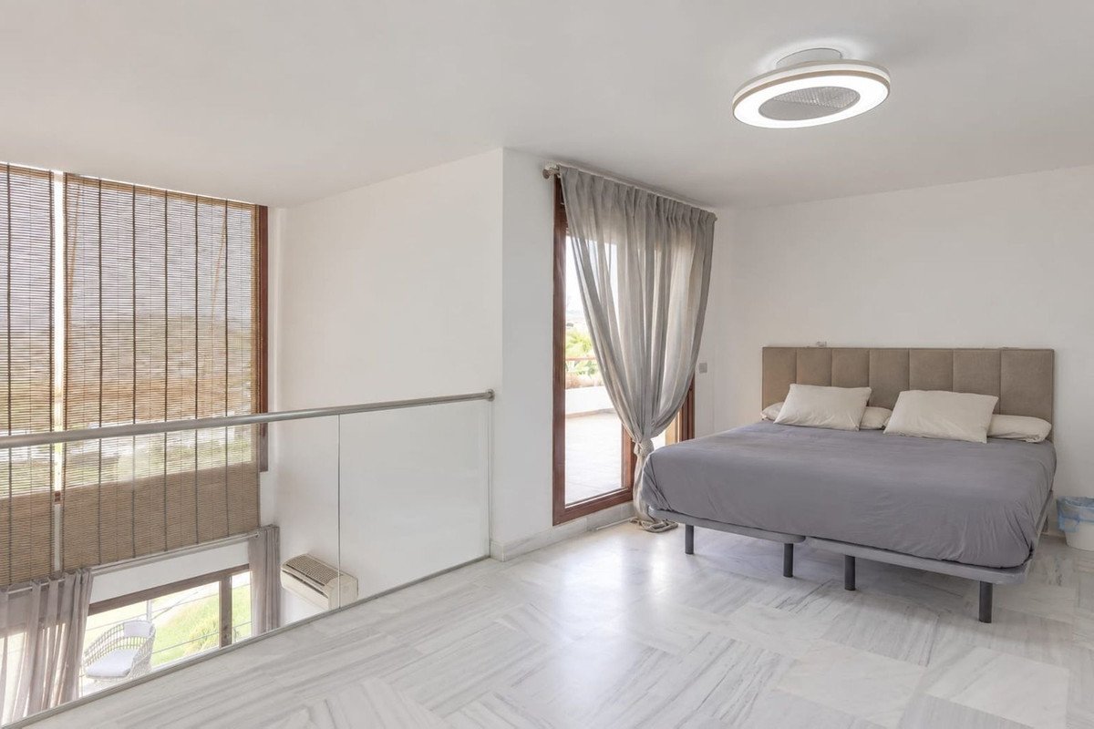 Spacious master bedroom with a large bed, balcony doors, and a view of the outdoors. Modern ceiling fan light.
