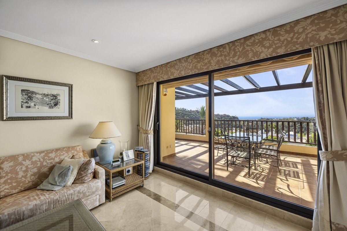 Living room with sofa, opening to a spacious balcony with sea view, outdoor dining table and chairs.