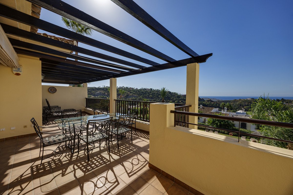 Spacious terrace with a dining table and chairs, overlooking a scenic landscape and the blue sea under a clear sky.