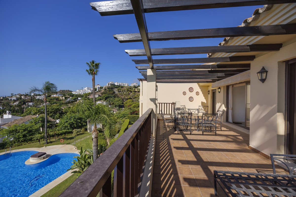 Spacious terrace with outdoor dining set, overlooking a swimming pool and lush green hillside with palm trees under a clear blue sky.