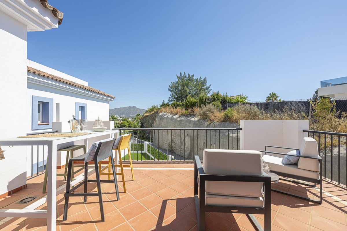 Terrace with outdoor seating, table, and chairs, offering a view of the landscape and distant mountains under a clear blue sky.