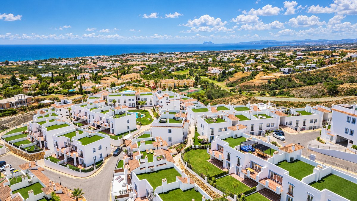 Modern white villas with green roofs, overlooking the blue sea and coastal landscape on a sunny day.