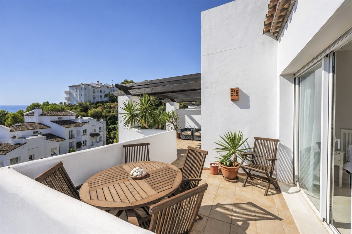 Terrace with wooden dining set and chairs, offering a view of white buildings and the sea under a clear blue sky.
