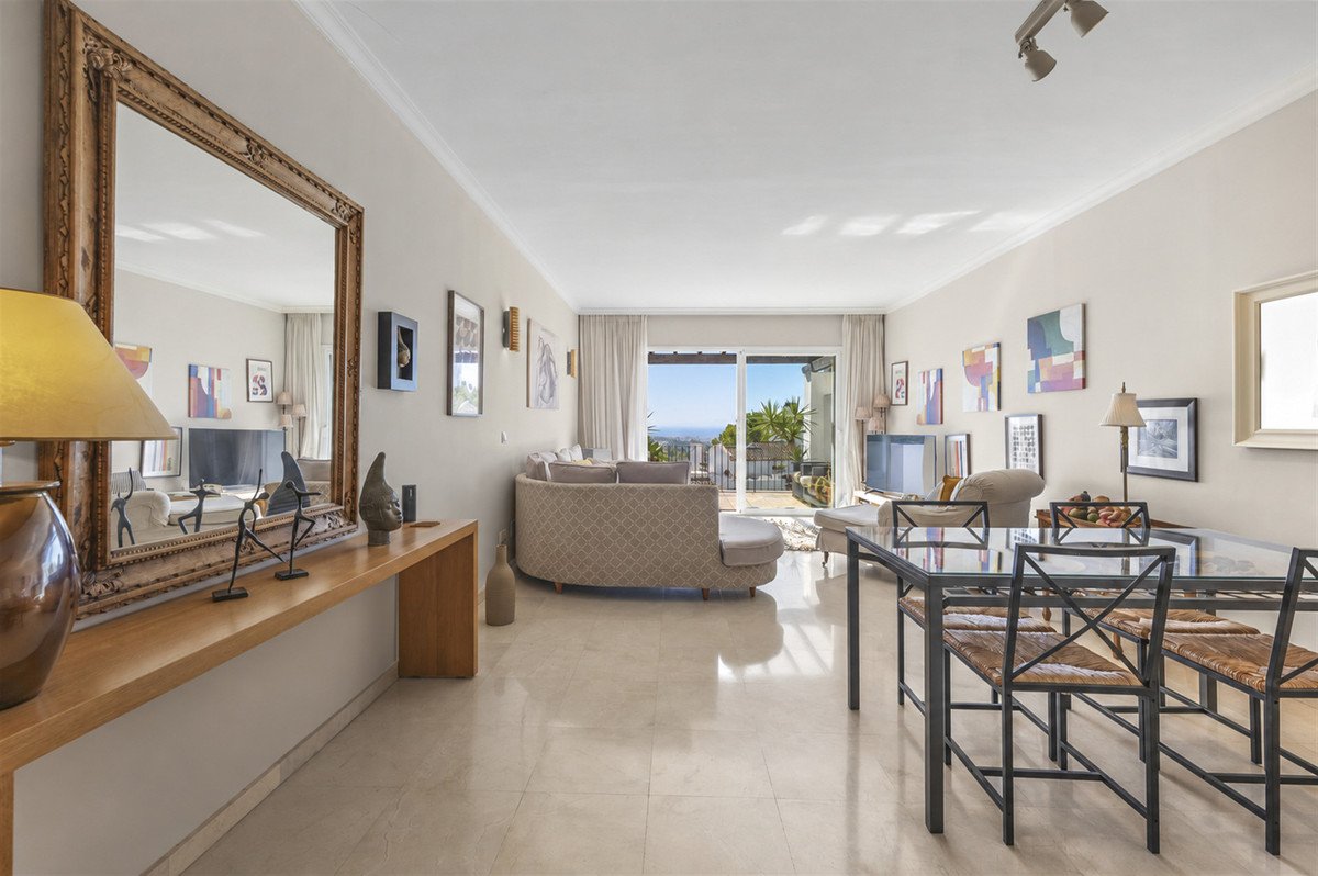 A spacious living and dining area with a curved sofa, dining table, and a balcony offering a sea view.