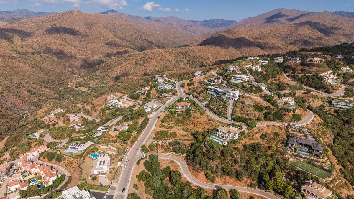Aerial view of luxury villas nestled in a mountainous landscape, featuring swimming pools and a tennis court.