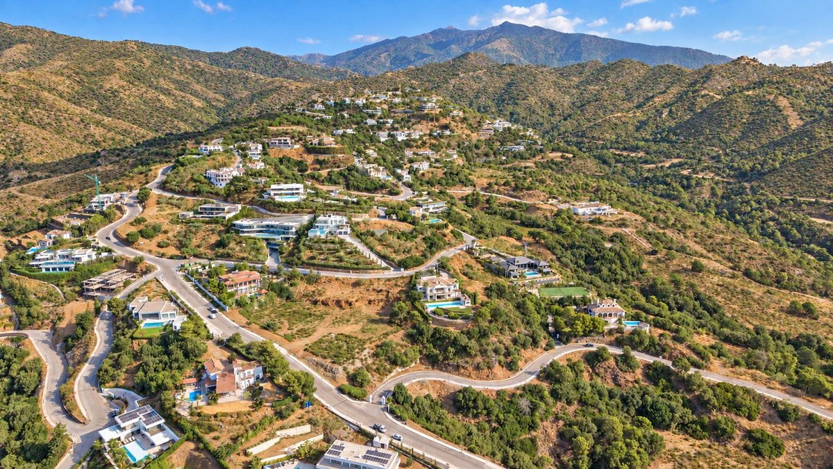 Aerial view of a luxury villa development nestled on a mountainside with winding roads and distant mountain ranges.