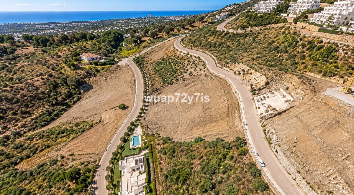 Aerial view of a hillside development with roads, houses, a pool, and the sea in the distance.