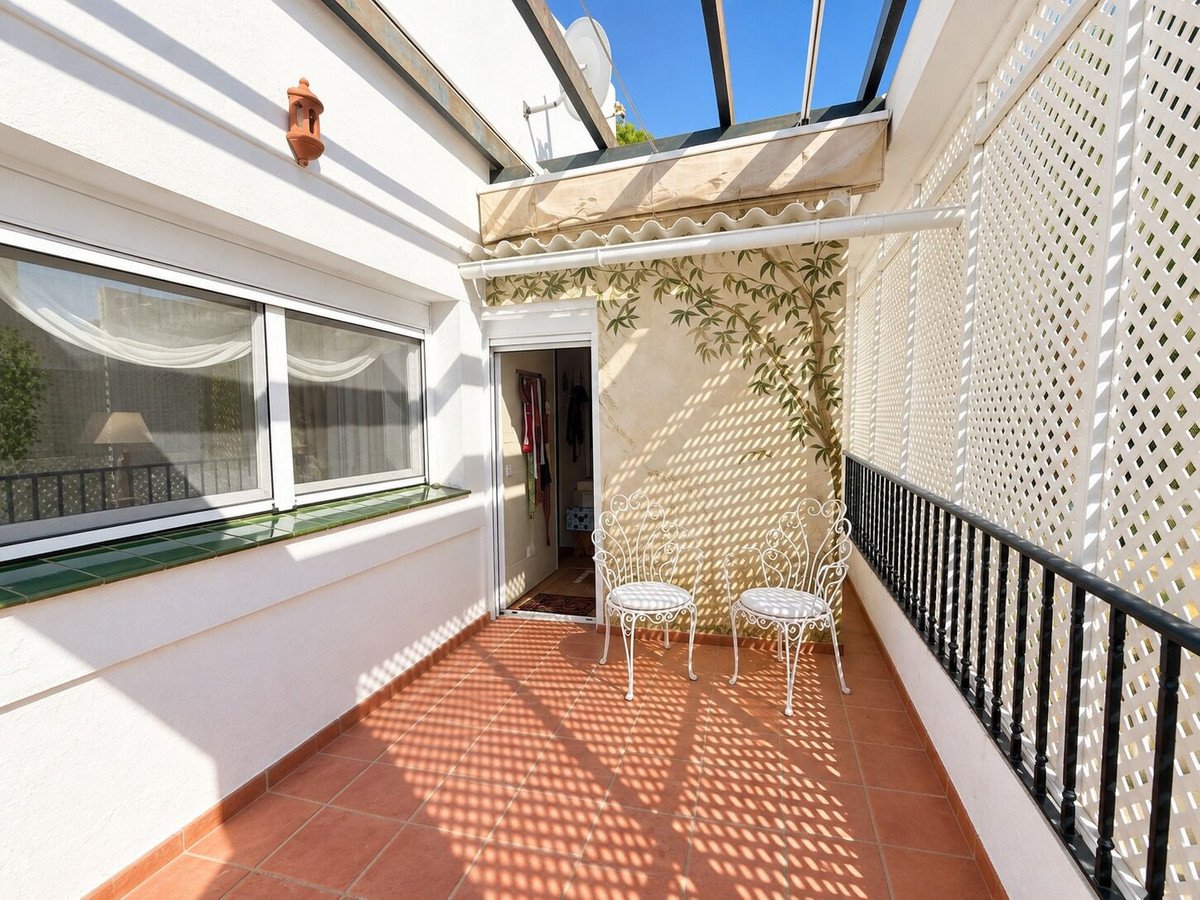 A covered terrace with terracotta tiles, two white chairs, and a decorative lattice screen fence panels offering privacy and decorative bamboo-or decoration.