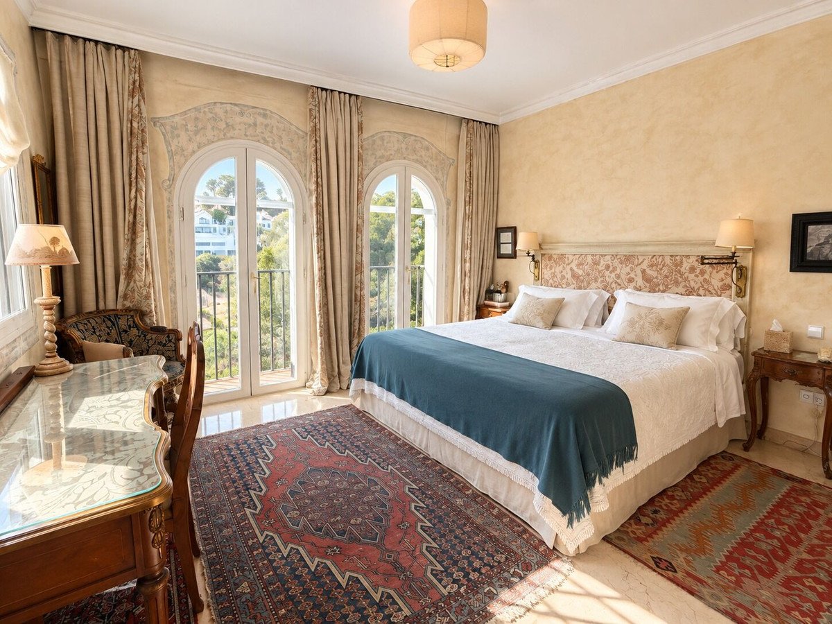 Elegant bedroom with a king-size bed, balcony access, and scenic views of greenery and buildings.