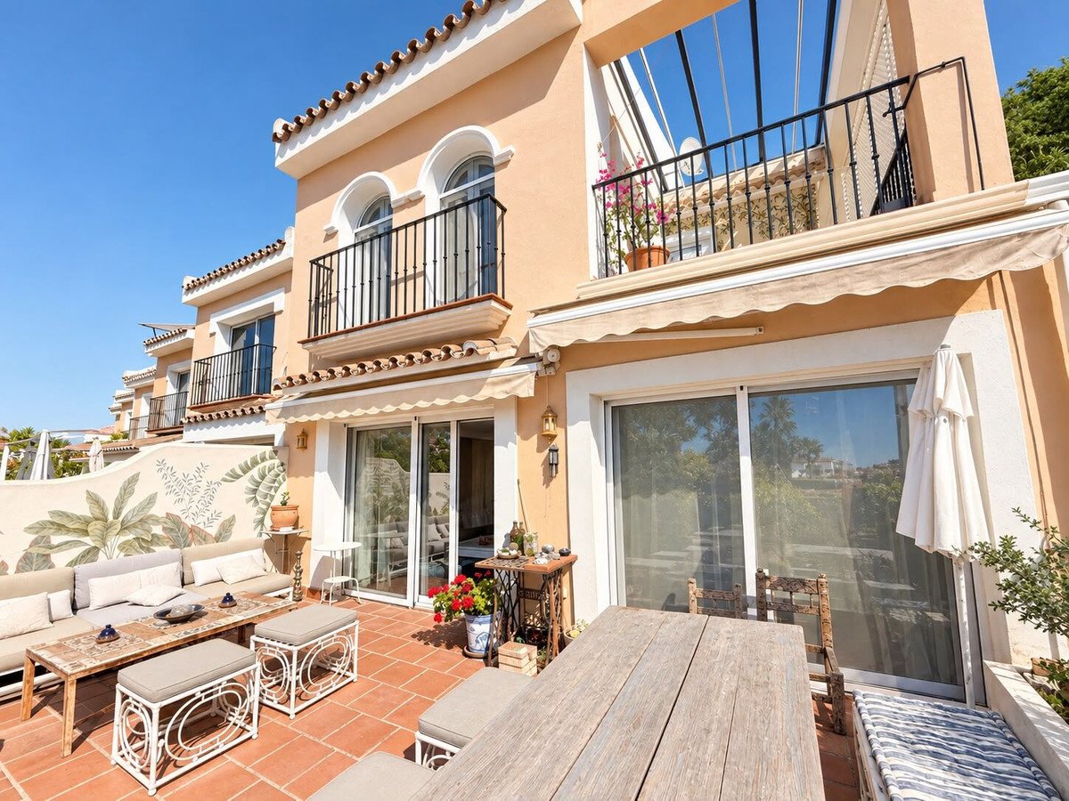 Spacious outdoor terrace with comfortable seating, a wooden dining table, and a view of the surrounding greenery under a clear blue sky.