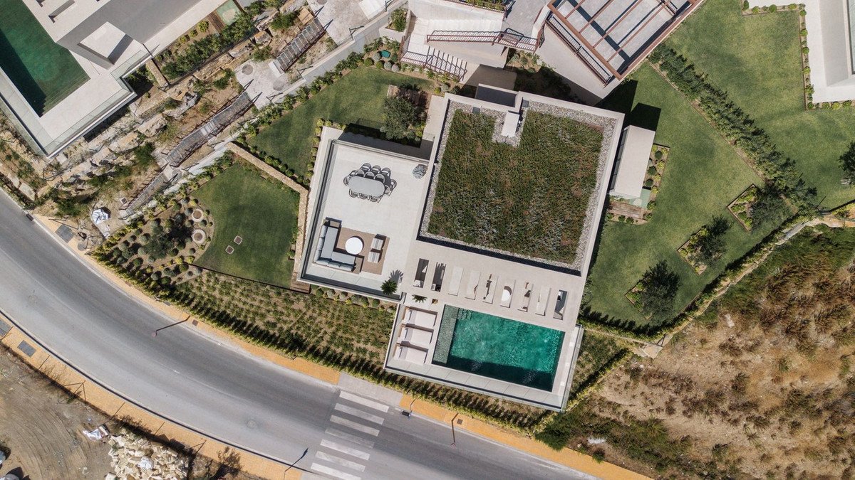 Aerial view of a modern villa with a swimming pool, sun loungers, and outdoor dining area on a terrace.