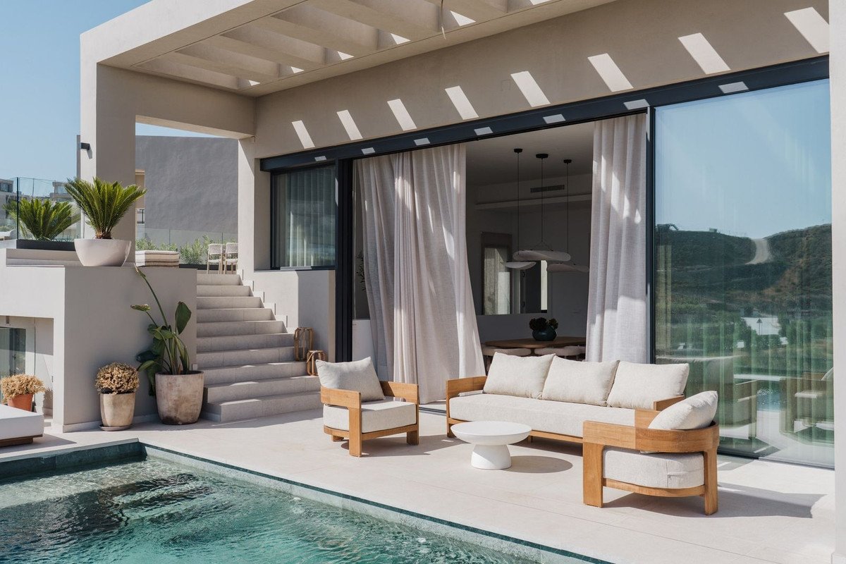 Modern patio with a swimming pool, outdoor sofa, armchair, and coffee table, with scenic hill views through sliding glass doors.