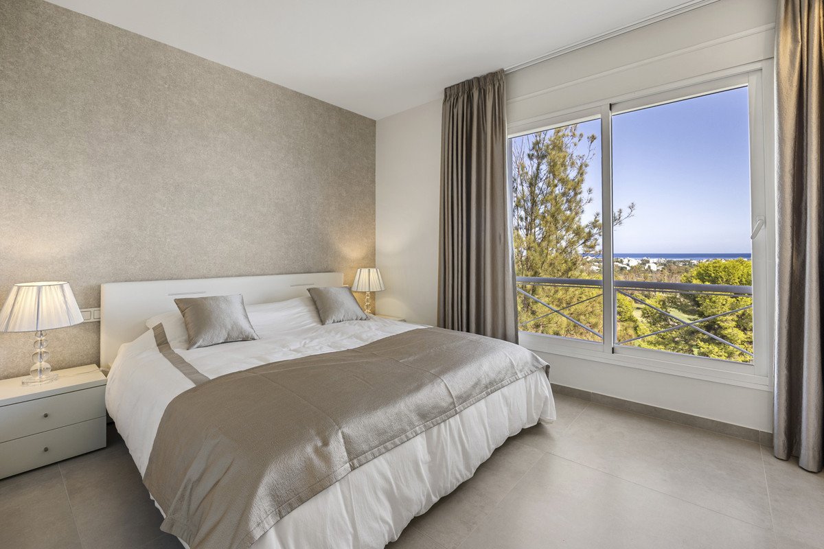 Bedroom with a large bed and a stunning view of the sea and trees from the window.