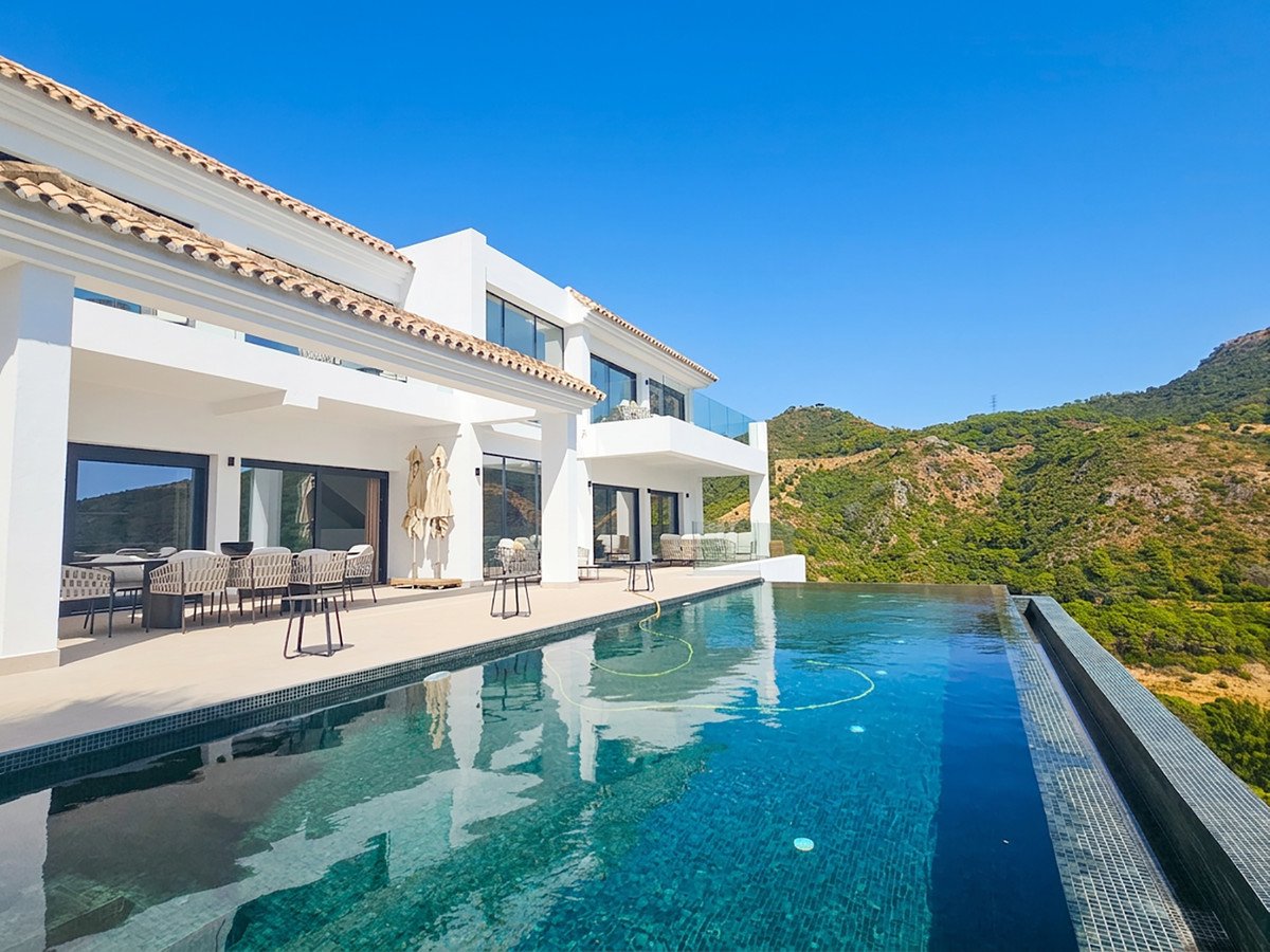 Modern villa with an infinity pool overlooking lush green mountains under a clear blue sky.