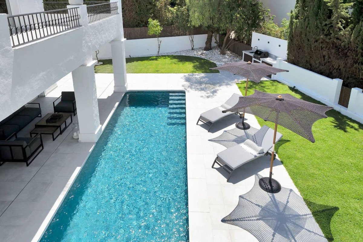 Luxury swimming pool with lounge chairs and umbrellas, outdoor seating area, and barbecue setup. Perfect for relaxation.