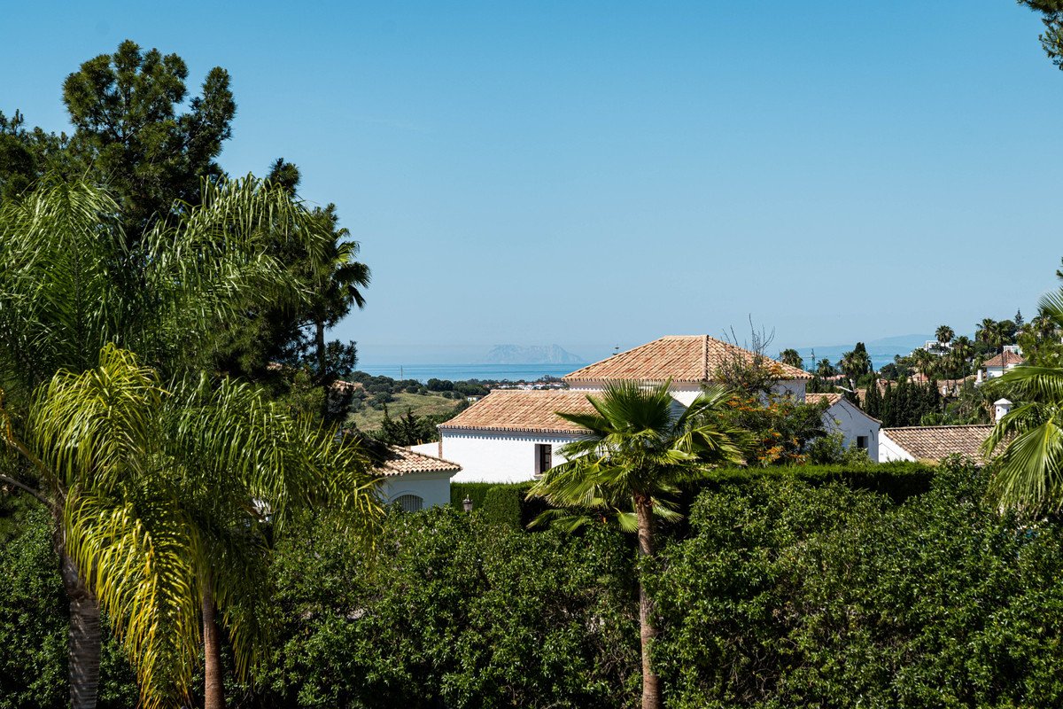 View of villas with tiled roofs surrounded by lush green trees and a distant view of the sea.