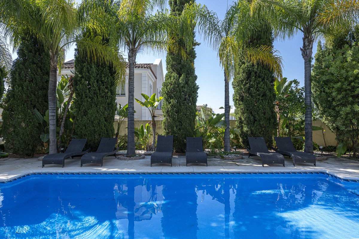Luxurious swimming pool with lounge chairs set amidst a lush tropical garden with palm trees and a villa in the background.