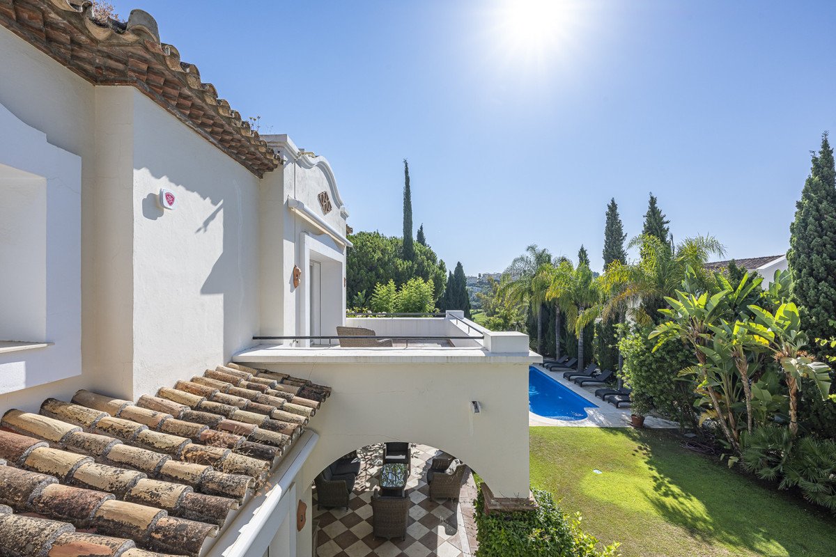 Terrace overlooking a swimming pool, lush garden, and palm trees under a clear blue sky.