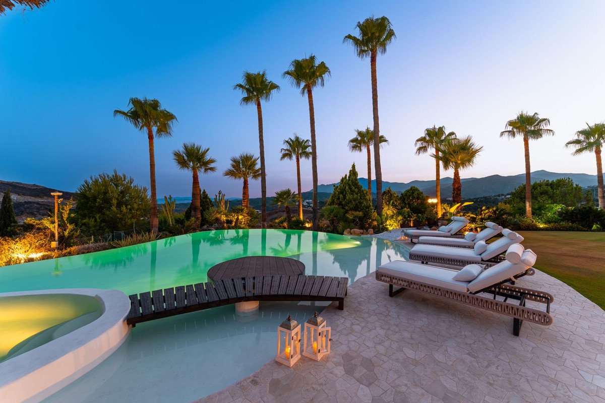 Infinity pool with lounge chairs and palm trees at twilight, offering a luxurious outdoor relaxation space.