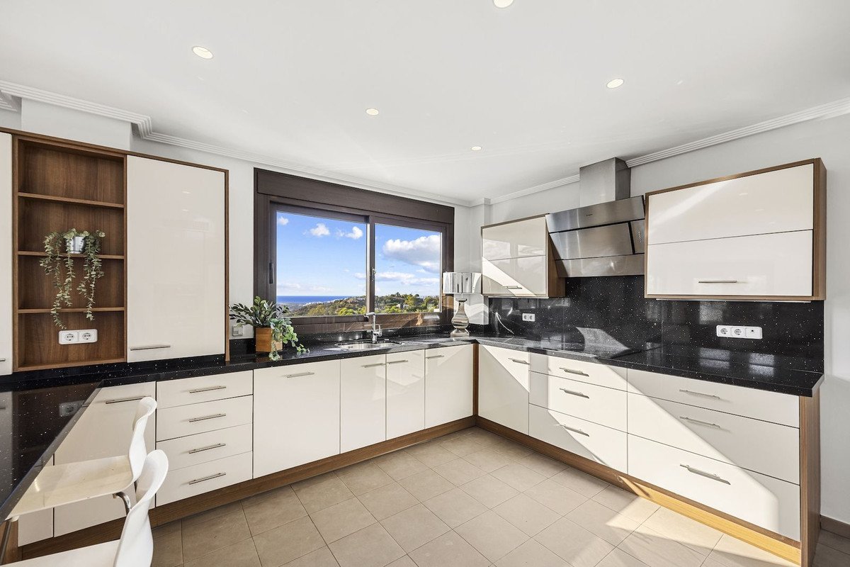 Modern white kitchen with black granite countertops and a large window offering a beautiful sea view.