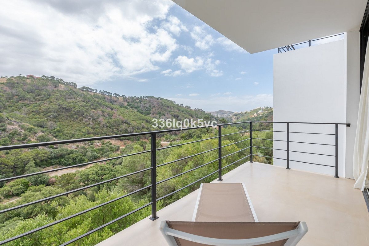 Modern balcony with a lounge chair offering stunning panoramic views of lush green mountains under a cloudy sky.