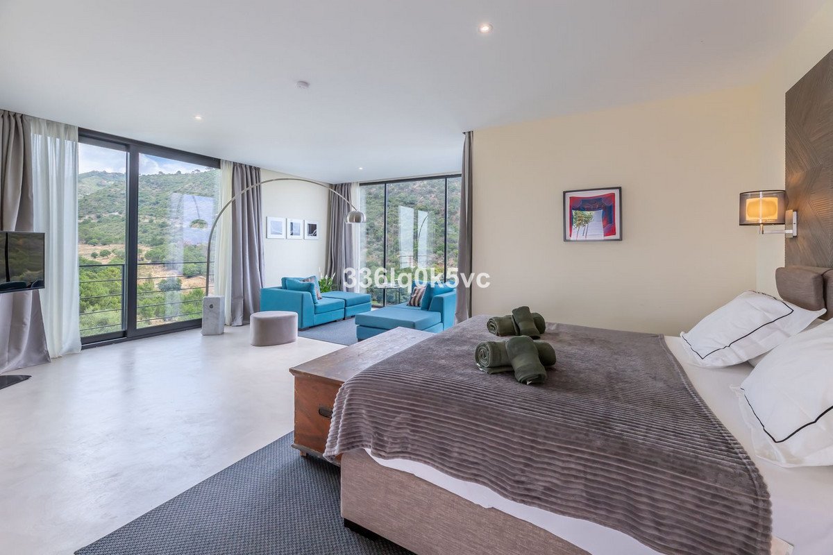Spacious bedroom with a sitting area, large windows showcasing a lush mountain view, and modern furnishings.