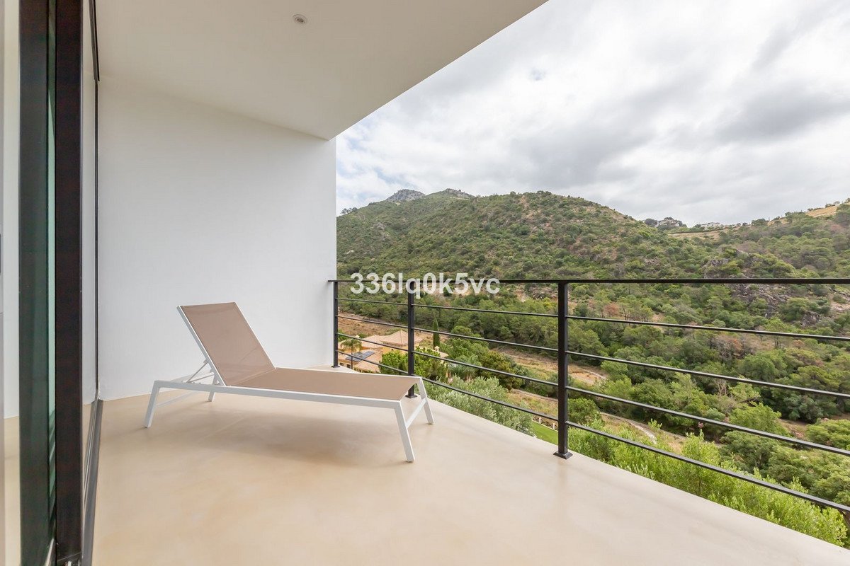 Modern balcony with a chaise lounge and a stunning view of green mountains under a cloudy sky.