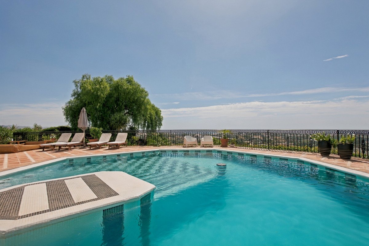 Luxurious outdoor swimming pool with lounge chairs, parasol, and a scenic view of the landscape under a clear blue sky.