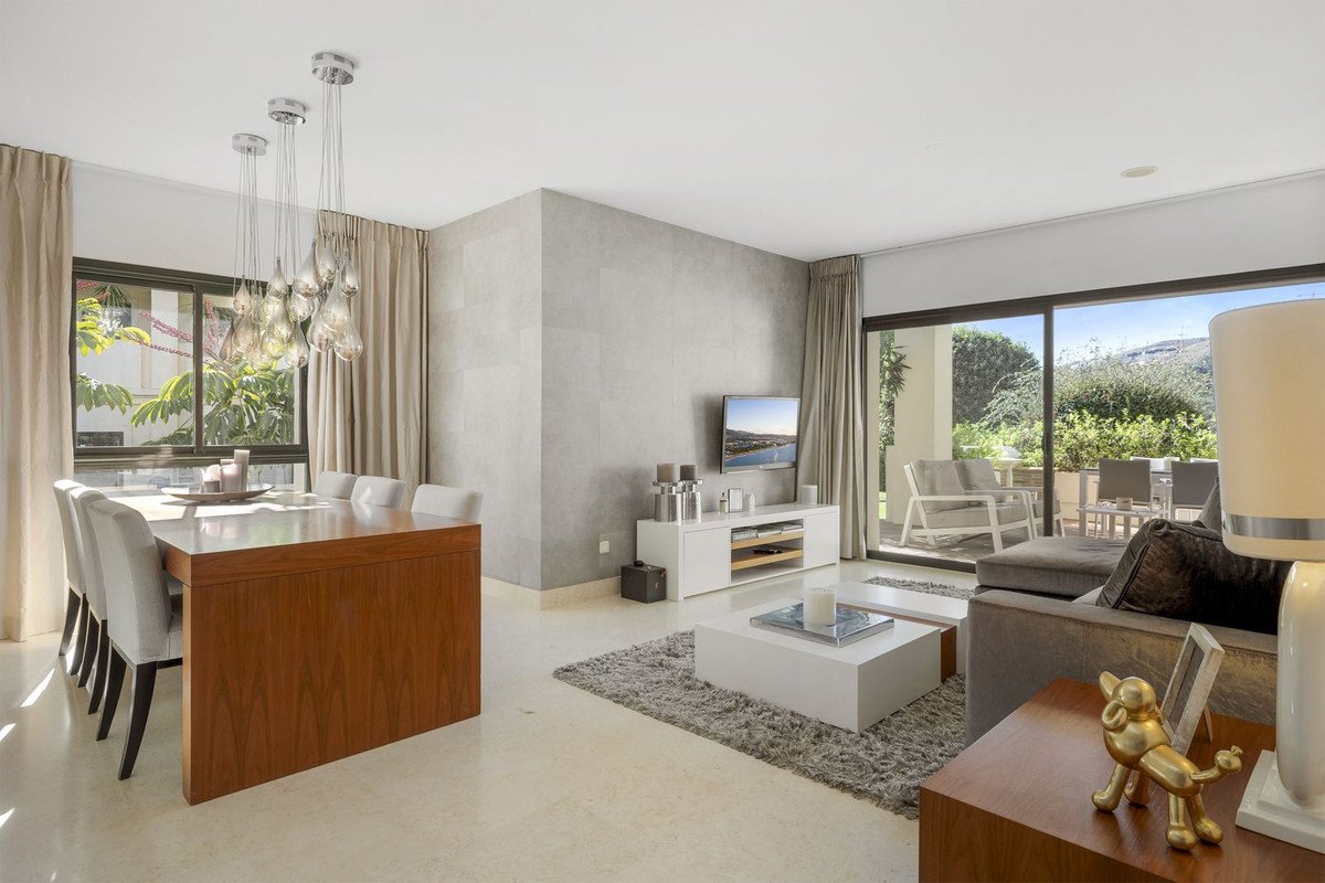 Modern living and dining area with large windows overlooking a patio and lush greenery, featuring stylish furniture and a TV.