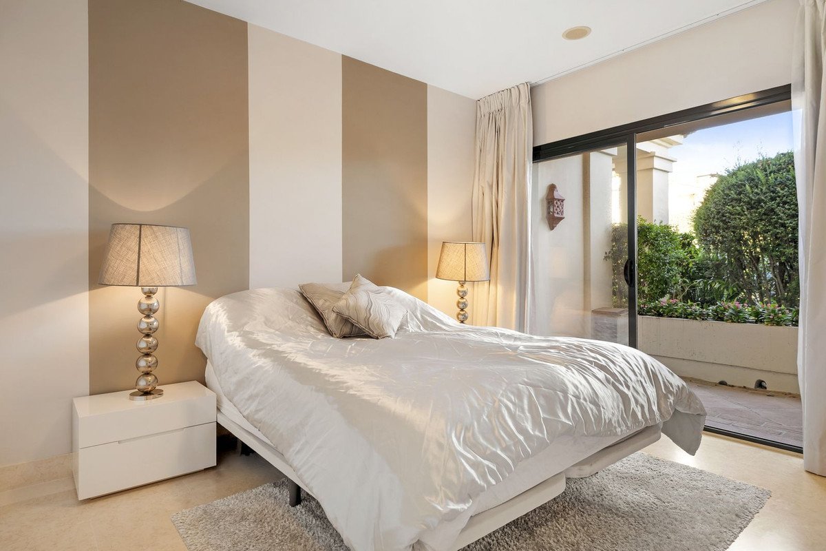 A bedroom with a king-sized bed, striped walls, bedside lamps, and sliding glass doors leading to a lush garden patio.