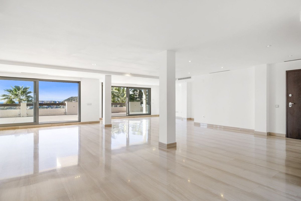Expansive, modern living room with floor-to-ceiling windows showcasing a balcony with sea and palm tree views.