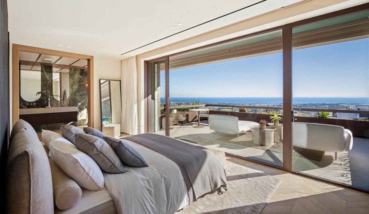Modern bedroom with a king-size bed and en-suite bathroom, opening to a balcony with sea and city views.