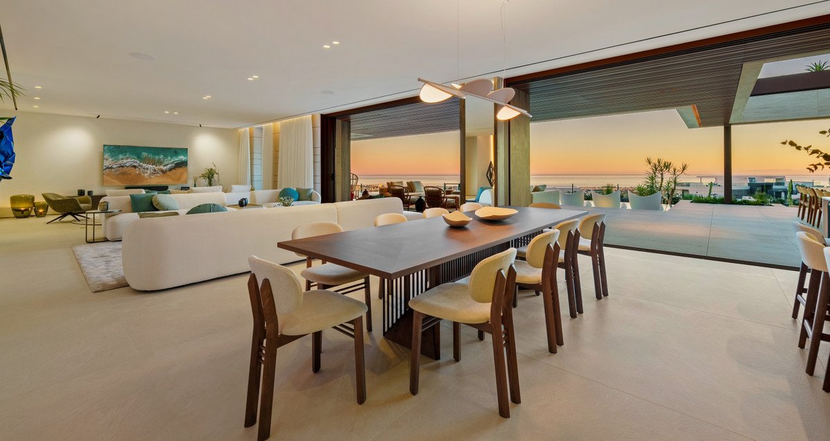 Modern dining and living area with ocean view, opening to a spacious terrace at sunset.