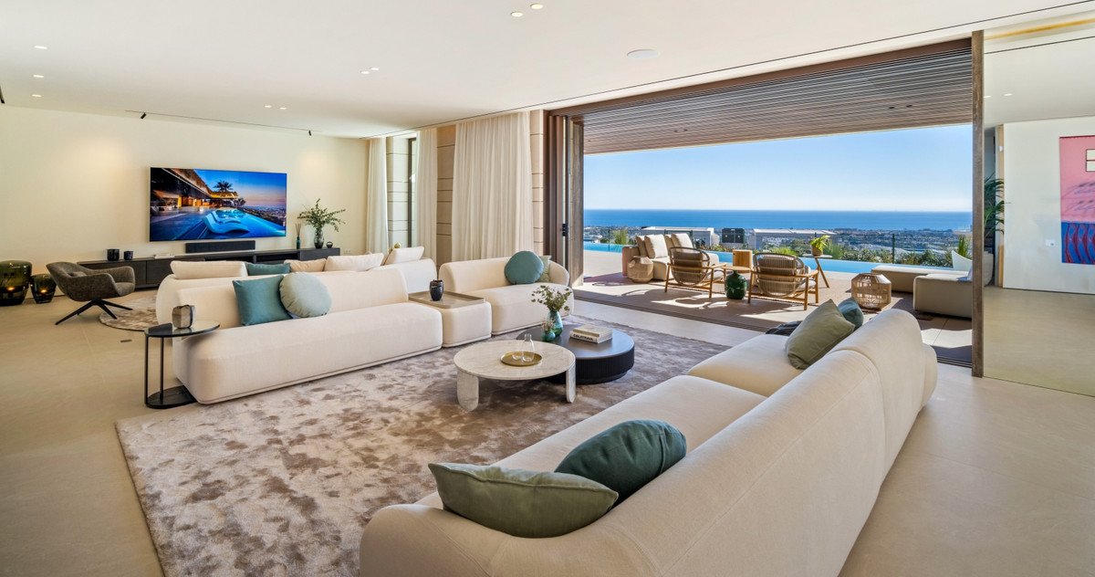 Spacious modern living room with plush sofas, large TV, and open-concept sliding doors leading to a patio with an ocean view.