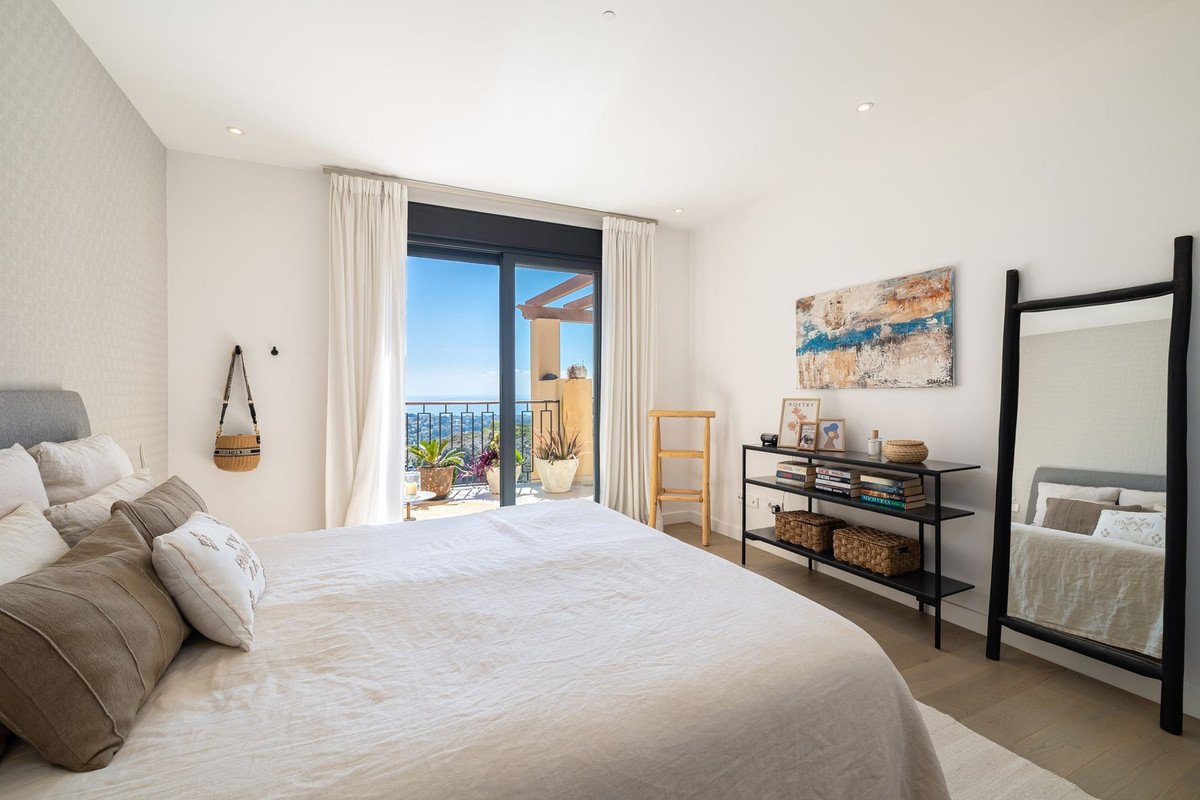 Bedroom with a large bed, a sliding glass door opening to a balcony with a sea view, and decorative shelves.