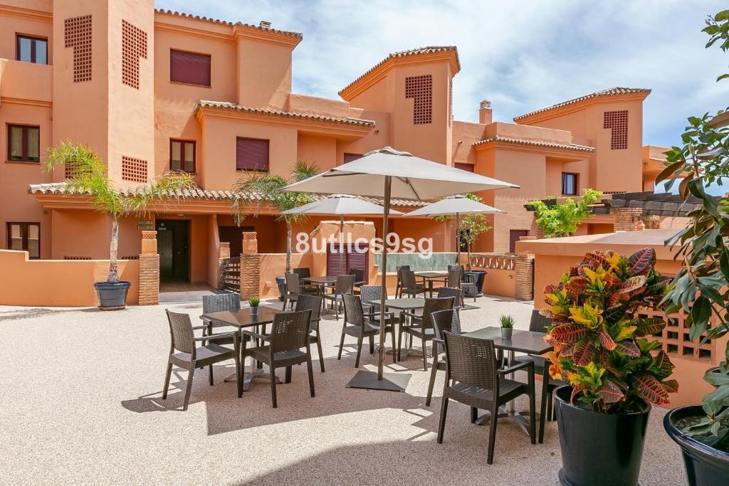 Outdoor dining area with tables and chairs under umbrellas, facing a residential building.