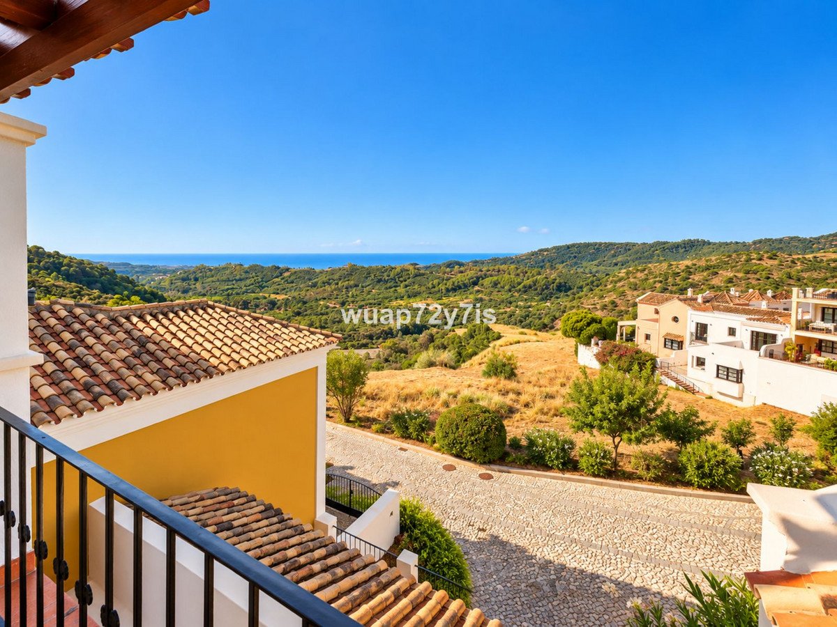 View from a balcony overlooking a Mediterranean landscape with rolling hills, distant sea, and white villas under-construction villas under a clear blue sky.