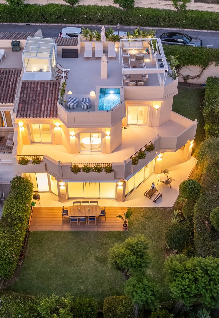 Luxury villa with a rooftop pool, lounge area, garden, and outdoor dining space, viewed from above at dusk.