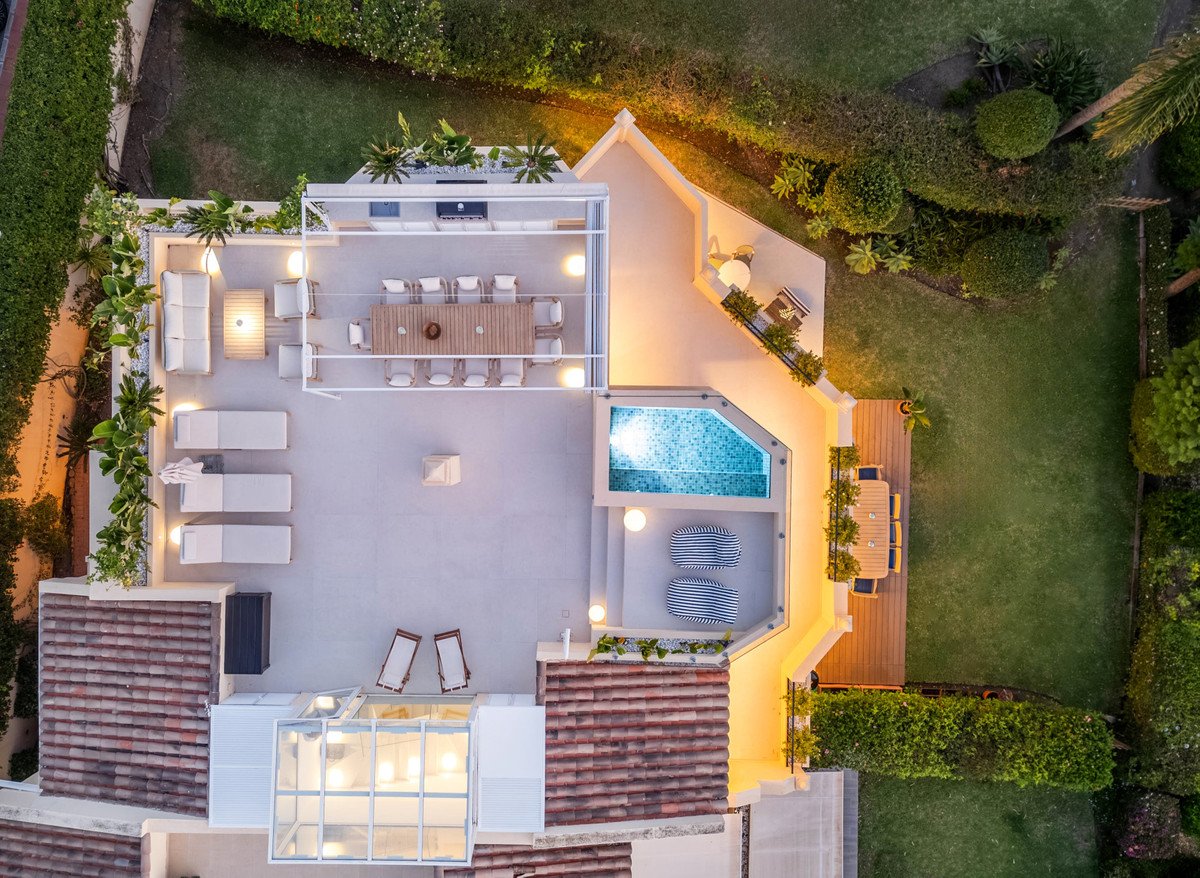 Aerial view of a modern luxury villa with a pool, dining area, lounge seating, and lush green garden.